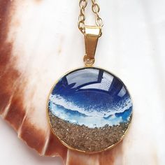 a necklace with an ocean scene in the center on a gold plated metal chain