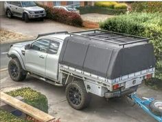 a truck with a trailer attached to it parked in front of some bushes and trees