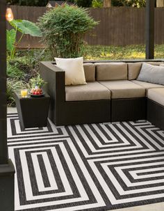 an outdoor living area with black and white rugs, couches, tables and potted plants