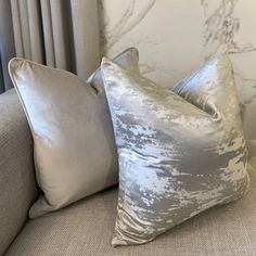 two silver pillows sitting on top of a couch