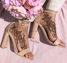 a woman's feet with henna tattoos on them and flowers in the background