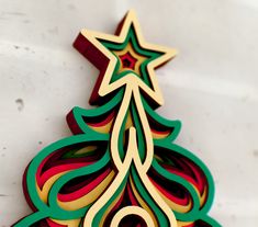 a christmas tree made out of colored paper on top of a white surface with an ornament in the shape of a star