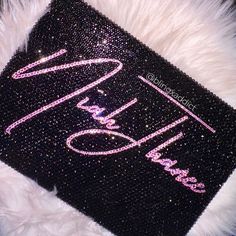 there is a black and pink sparkle case on top of a white fur rug with the word hello kitty written in cursive writing