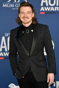 a man in a tuxedo smiles for the camera on the red carpet at an awards event