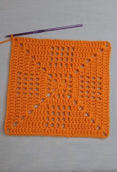 an orange crocheted square with a purple knitting needle