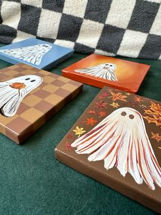 four painted coasters sitting on top of a green tablecloth covered floor next to a black and white checkered couch