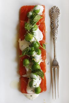 a piece of salmon with cream cheese and green peas on it next to a fork