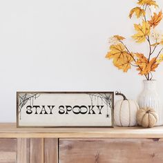 a wooden sign that says stay spooky next to some pumpkins on a dresser