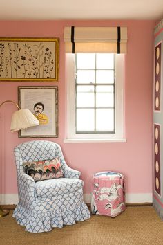 a chair and ottoman in front of a pink wall with pictures on the wall behind it