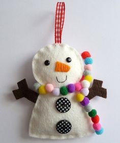 a felt snowman ornament hanging on a white wall with multicolored pom - poms