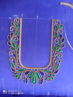 an ornate gold necklace with green and blue beads is displayed on a purple background,