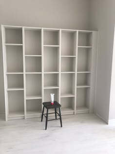 an empty white bookcase with a small stool in front of it on the floor