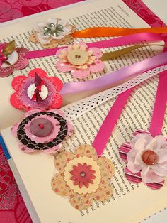 some paper flowers and hearts are on top of a book with ribbons, buttons and pins