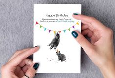 two hands holding a birthday card with an image of a raccoon