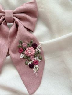 a pink bow with flowers on it laying on top of a white cloth covered bed