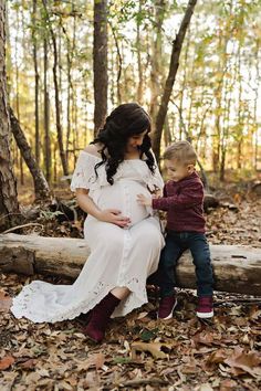 a pregnant woman sitting next to a little boy in the woods