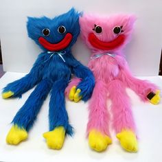 two colorful stuffed animals sitting next to each other on a white surface with one holding the other's hand