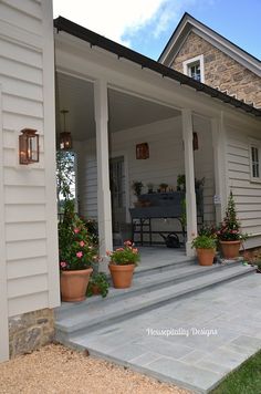 a porch with potted plants and flowers on the steps leading up to a house