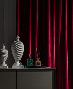 two white vases sitting on top of a black cabinet next to a red curtain