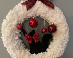 a white wreath with red ornaments hanging from it's sides and a black silhouette on the front