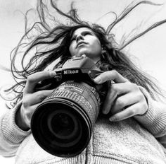 black and white photograph of a woman holding a camera with her hair blowing in the wind