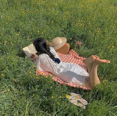 a woman laying in the grass reading a book with her legs crossed and hat on her head