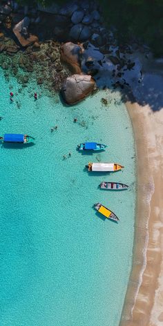 several small boats floating on top of a blue body of water next to a sandy beach