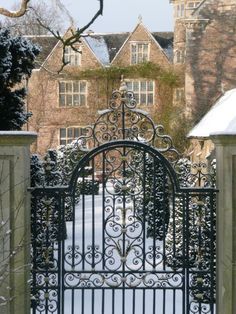 an iron gate in front of a brick building with snow on the ground and trees