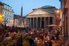 many people are sitting at tables outside in front of an old building with columns and pillars