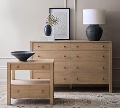 a wooden dresser sitting next to a black bowl on top of a white table lamp