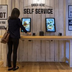 a woman standing in front of two televisions with food on them and the words order here, self service