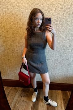 a woman taking a selfie in front of a mirror holding a red purse and wearing white tennis shoes