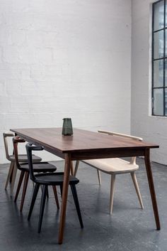 a wooden table with chairs around it in front of a white brick wall and window