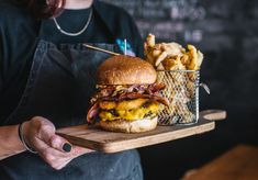 a person holding a tray with a large sandwich and french fries on it in front of a chalkboard wall