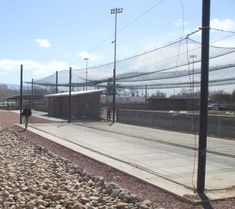 a man walking down a sidewalk next to a tennis court covered in rocks and netting