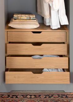 a chest of drawers with clothes hanging on the wall behind it and a rug underneath