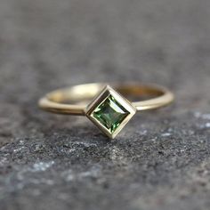 a yellow gold ring with a green diamond on the top, sitting on a stone surface