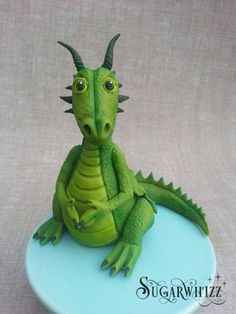 a green toy dragon sitting on top of a blue plate with it's eyes wide open