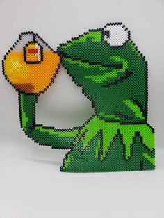 the kermie frog is holding an orange object in his hand and it looks like he