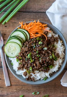 a bowl filled with rice, cucumbers and ground beef next to a fork