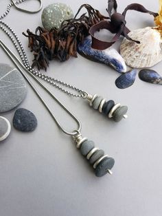 several different necklaces are laying on a table with rocks and seashells in the background