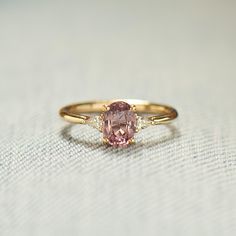 a pink diamond ring sitting on top of a white cloth covered table with a light colored background