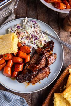 a plate with meat, carrots and coleslaw on it next to bread