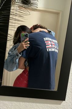 a man and woman taking a selfie in front of a mirror with palm leaves