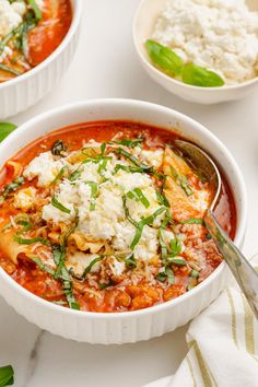 two bowls filled with pasta and cheese on top of a white tablecloth next to other dishes