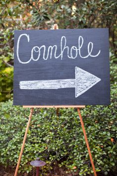 a blackboard sign with the words comhole and an arrow pointing to the right