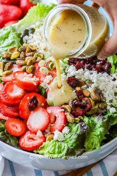 someone pouring dressing onto a salad with strawberries and nuts on the side in a bowl