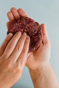 two hands holding a piece of food in front of the camera on a gray background