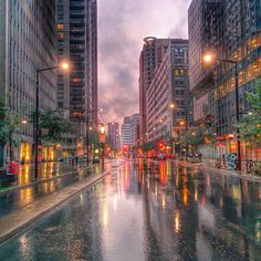 the city street is wet and it's raining at night with buildings in the background