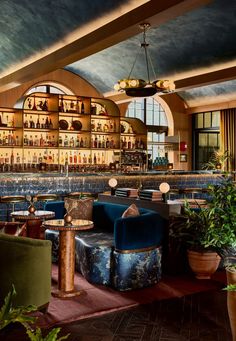 the interior of a bar with blue velvet chairs and potted plants in front of it